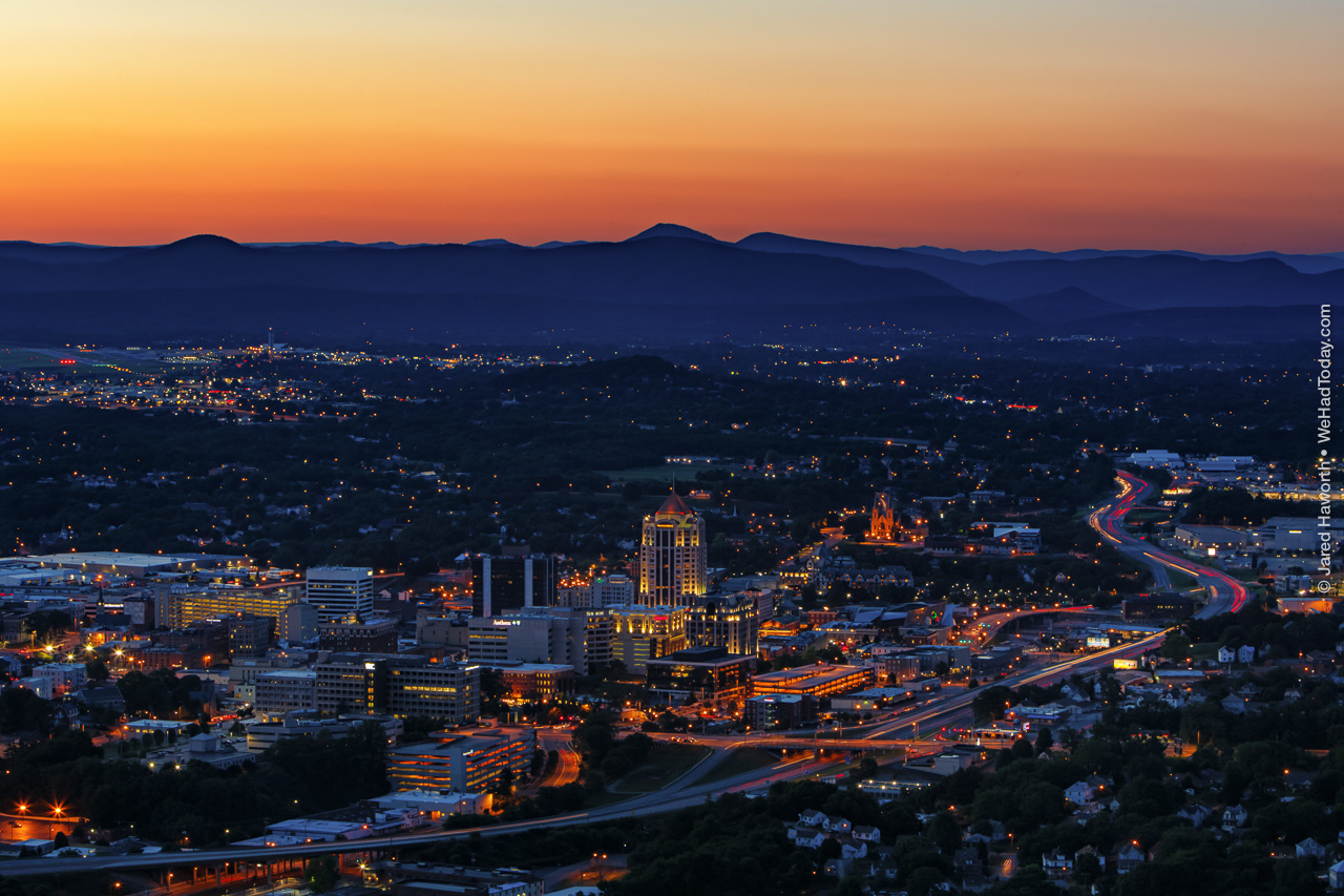 The setting sun lights the sky on fire as the lights of Roanoke glow in the valley below.