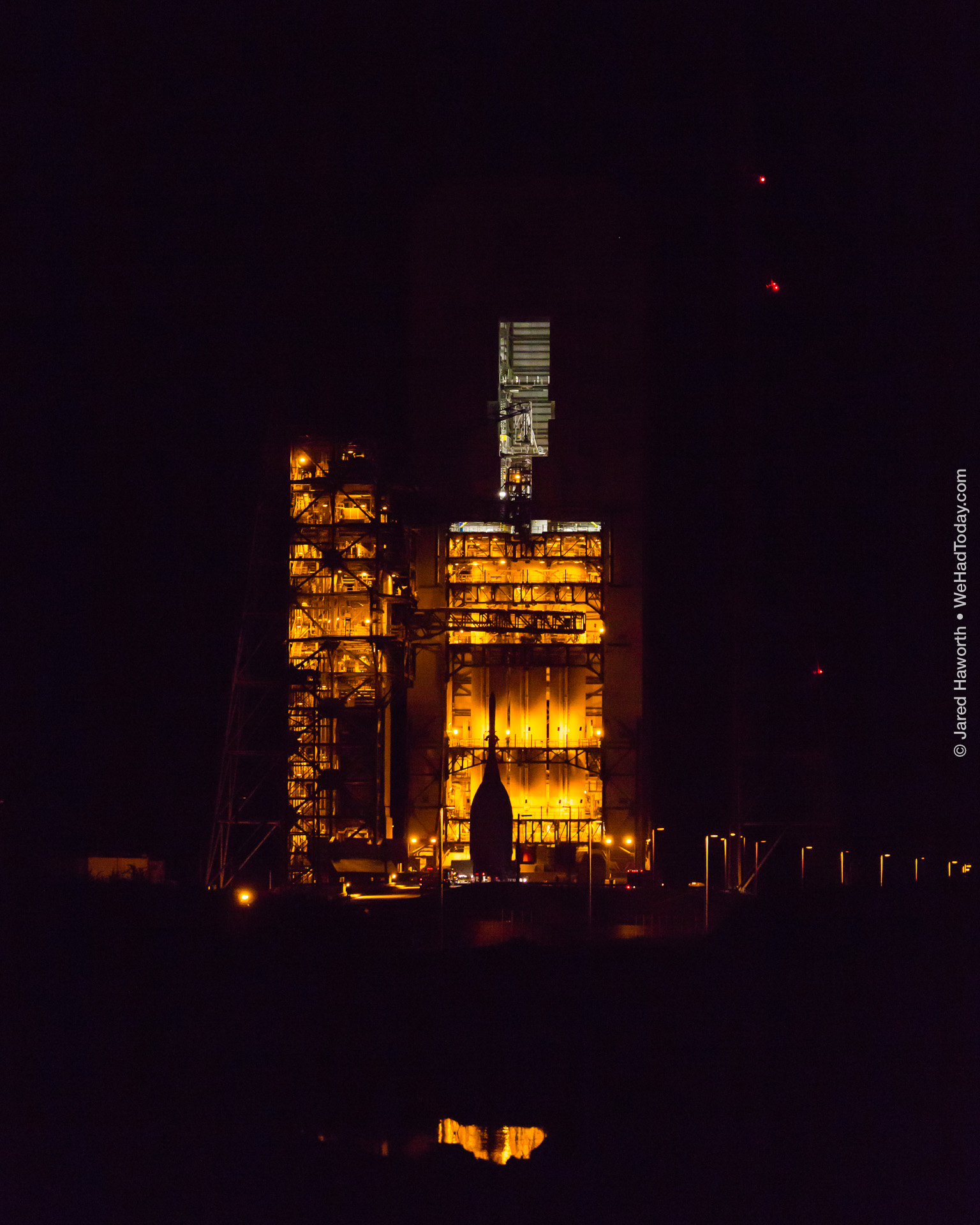 The Orion spacecraft arrives at Space Launch Complex 37B, and is seen in silhouette against the Delta IV Heavy launch vehicle within the mobile service tower.