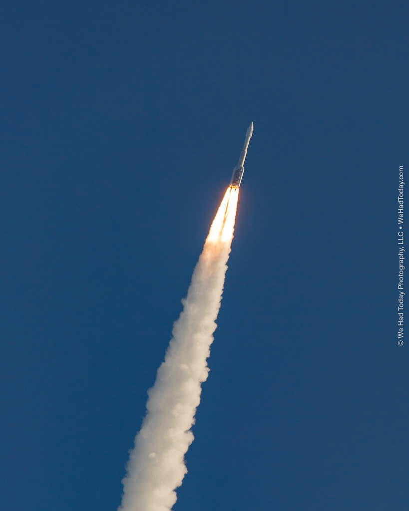 Twin solid rocket boosters frame the RD-180 main engine exhaust as the Atlas V soars through a clear blue sky.